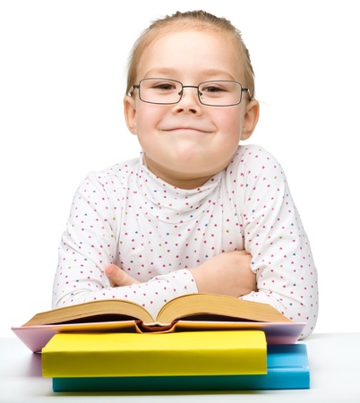 Cute cheerful little girl reading book while wearing glasses, isolated over whiteの写真素材