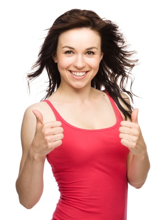 Young woman dressed in red is showing thumb up gesture using both hands, isolated over whiteの写真素材