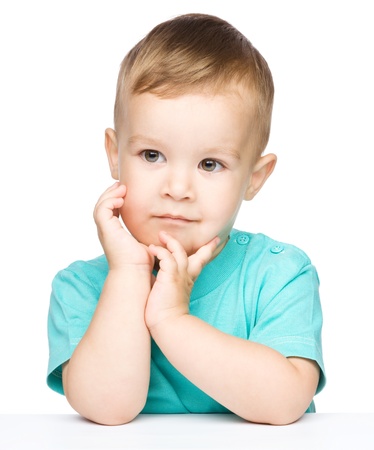 Portrait of a cute little boy looking at something while supporting his head with both hands, isolated over whiteの写真素材