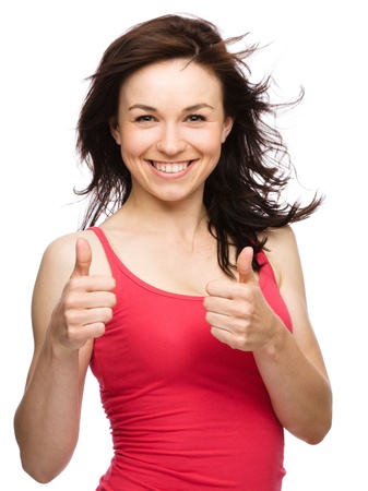 Young woman dressed in red is showing thumb up gesture using both hands, isolated over whiteの写真素材