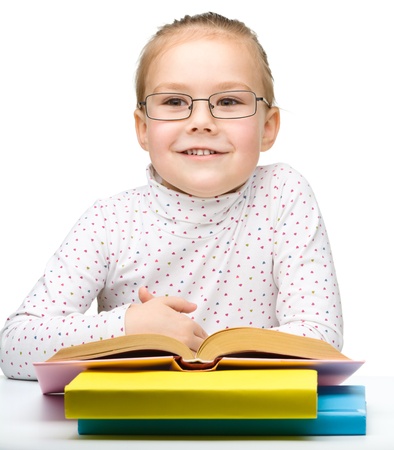 Cute cheerful little girl reading book while wearing glasses, isolated over whiteの写真素材