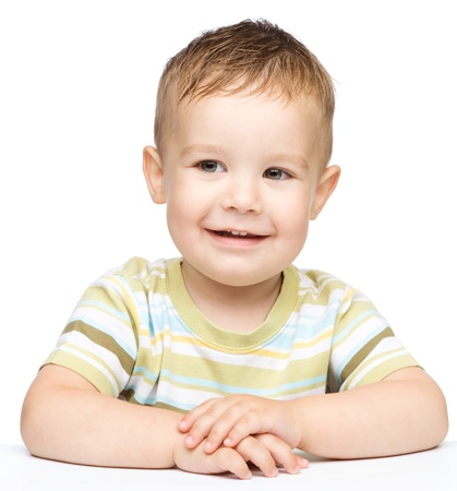 Portrait of a cute cheerful little boy, who is smiling while sitting at table, isolated over whiteの写真素材