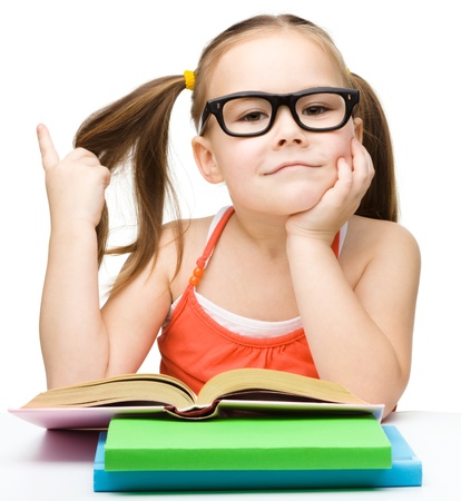 Cute cheerful little girl reading book while wearing glasses and waving her hair, isolated over whiteの写真素材