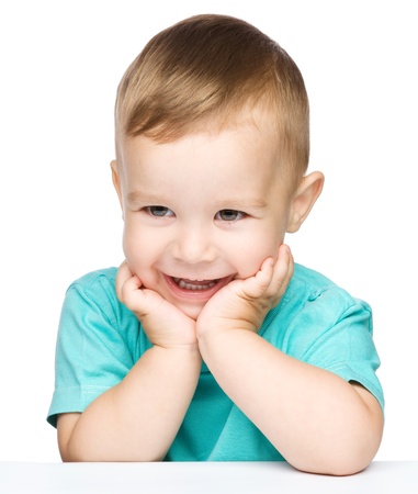 Portrait of a cute cheerful little boy, who is smiling while sitting at table, isolated over whiteの写真素材