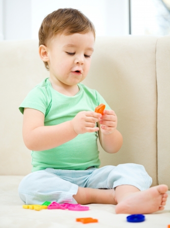Cute little boy playing with toys while sitting on a couch, indoor shootの写真素材