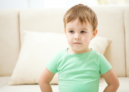 Cute little boy is standing in front of a sofaの写真素材
