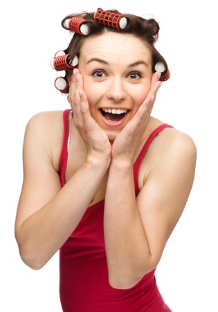 Young woman is holding her face in astonishment while wearing hair-rollers, isolated over whiteの写真素材
