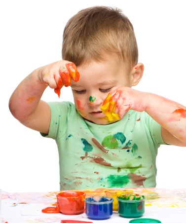 Portrait of a cute little boy playing with paints, isolated over whiteの写真素材