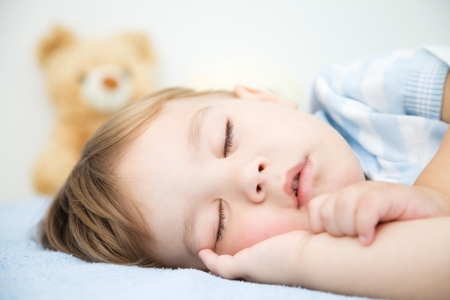 Cute little boy is sleeping in front of his teddy bearの写真素材