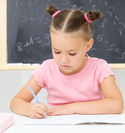 Cute little girl is writing using a pen in preschoolの写真素材