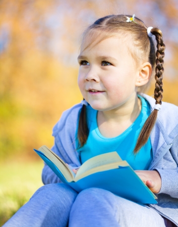 Cute little girl is reading a book outdoorsの写真素材