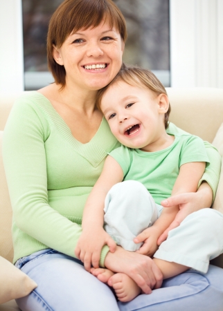 Mother is having fun with her son while sitting on a couchの写真素材