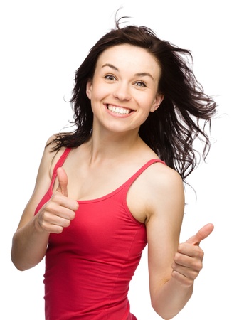 Young woman dressed in red is showing thumb up gesture using both hands, isolated over whiteの写真素材