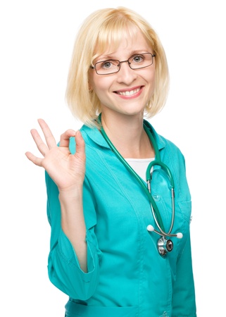 Portrait of a happy young attractive woman in doctor uniform showing OK sign, isolated over whiteの写真素材