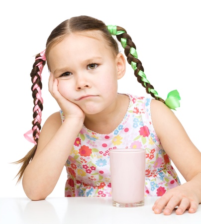Gloomy little girl does not want to drink milk, isolated over whiteの写真素材
