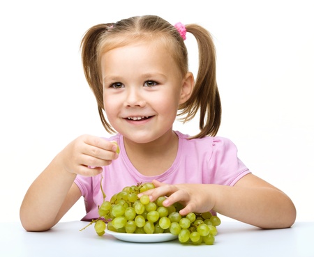 Little girl is eating grapes, isolated over whiteの写真素材