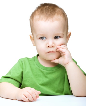 Portrait of a cute little boy sitting at table supporting his head with hands, isolated over whiteの写真素材