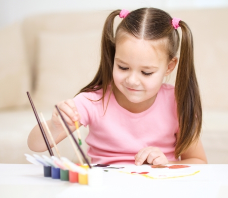 Cute cheerful child play with paints while sitting at tableの写真素材