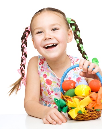 Little girl with basket full of colorful eggs preparing for Easter, isolated over whiteの写真素材