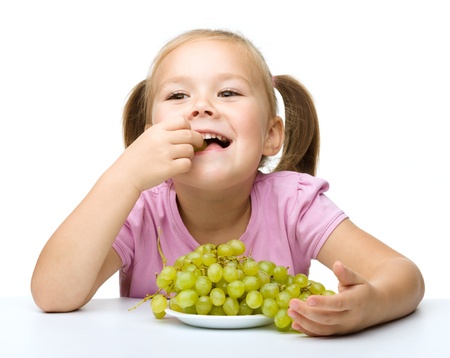 Little girl is eating grapes, isolated over whiteの写真素材