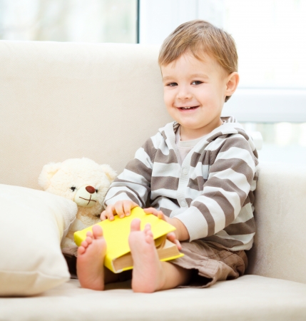 Little boy is reading book while sitting on couch, indoor shootの写真素材