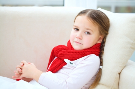 Ill little girl is laying on sofa with thermometer under her armの写真素材