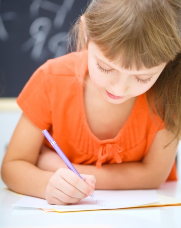 Cute little girl is writing using a pen in preschoolの写真素材