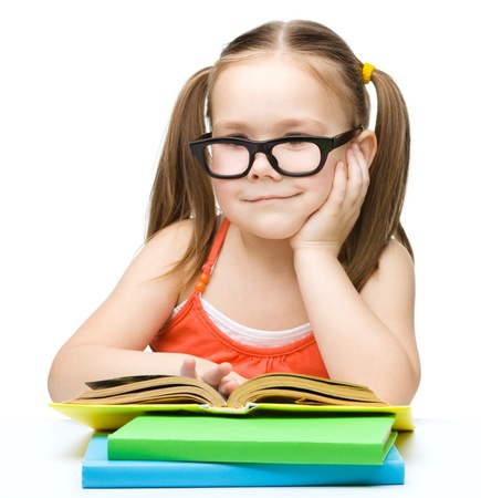 Cute little girl is reading a book while wearing glasses, isolated over whiteの写真素材