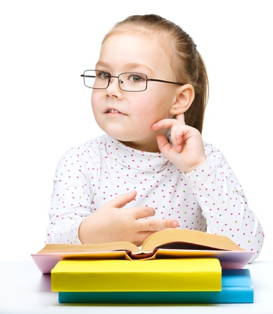Cute little girl with books and glasses holding hand near her ear like listening to something, isolated over whiteの写真素材