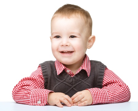 Portrait of a cute little boy sitting at table, isolated over whiteの写真素材