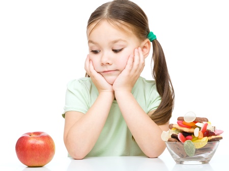 Cute little girl choosing between apples and sweets, isolated over whiteの写真素材