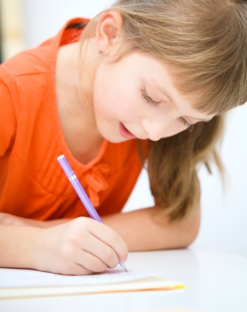 Cute little girl is writing using a pen in preschoolの写真素材