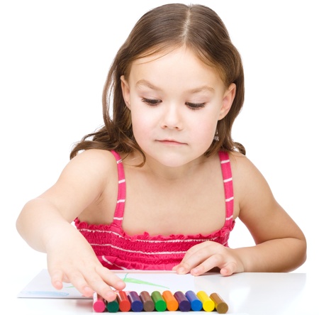 Little girl is drawing using colorful crayons while sitting at table, isolated over whiteの写真素材