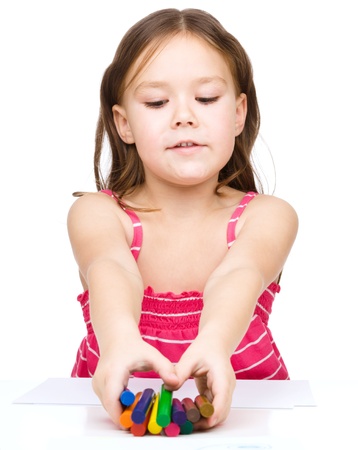 Little girl is drawing using color crayons while sitting at table, isolated over whiteの写真素材