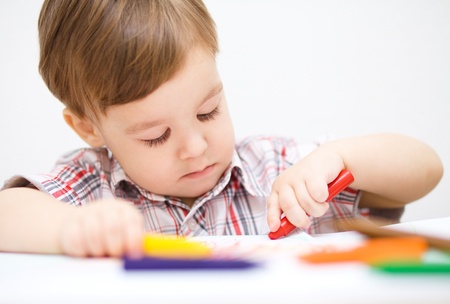 Little boy is drawing on white paper using crayonの写真素材