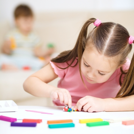 Little girl is playing with plasticine, her mother and brother at the backgroundの写真素材