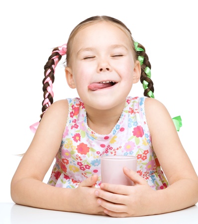 Cute little girl is licking her lips while drinking milk, isolated over whiteの写真素材