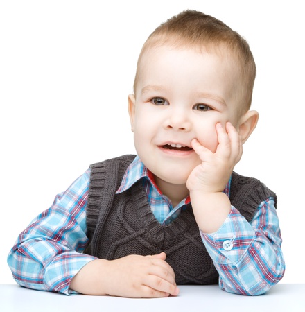 Portrait of a cute little boy sitting at table supporting his head with hands, isolated over whiteの写真素材