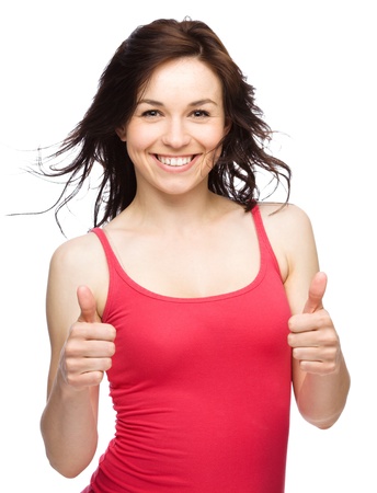 Young woman dressed in red is showing thumb up gesture using both hands, isolated over whiteの写真素材