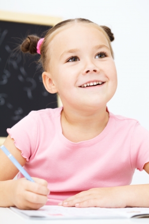 Cute little girl is writing using a pen in preschoolの写真素材