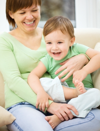 Mother is having fun with her son while sitting on a couchの写真素材