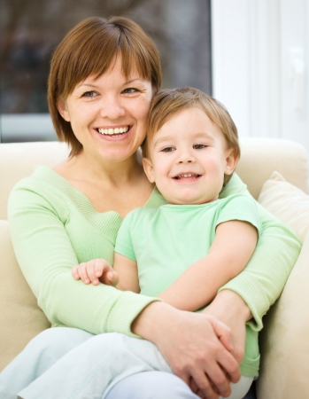 Mother is having fun with her son while sitting on a couchの写真素材