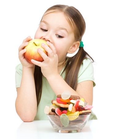 Cute little girl choosing between apples and sweets, isolated over whiteの写真素材