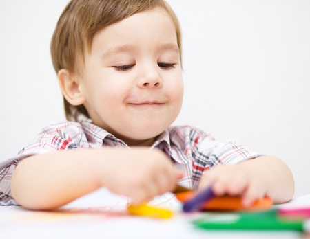Little boy is drawing on white paper using crayonの写真素材
