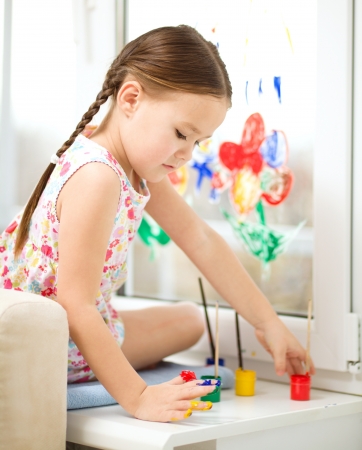 Portrait of a cute cheerful girl playing with paints on windowの写真素材