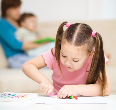 Little girl is playing with plasticine, her mother and brother at the backgroundの写真素材