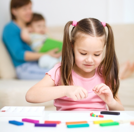 Little girl is playing with plasticine, her mother and brother at the backgroundの写真素材