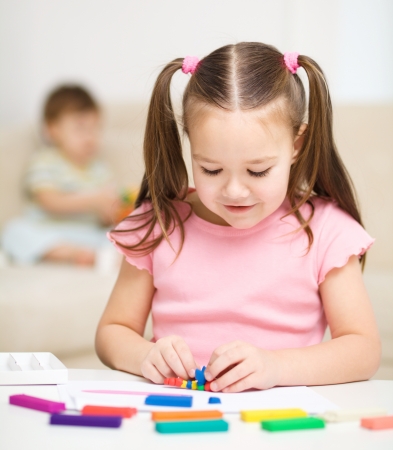 Little girl is playing with plasticine, her brother at the backgroundの写真素材
