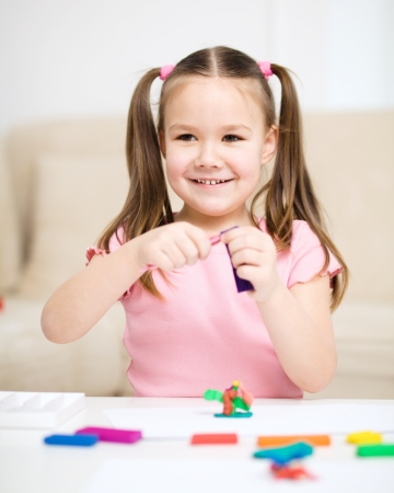Little girl is playing with plasticine while sitting at tableの写真素材