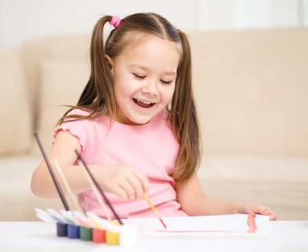 Cute cheerful child play with paints while sitting at tableの写真素材